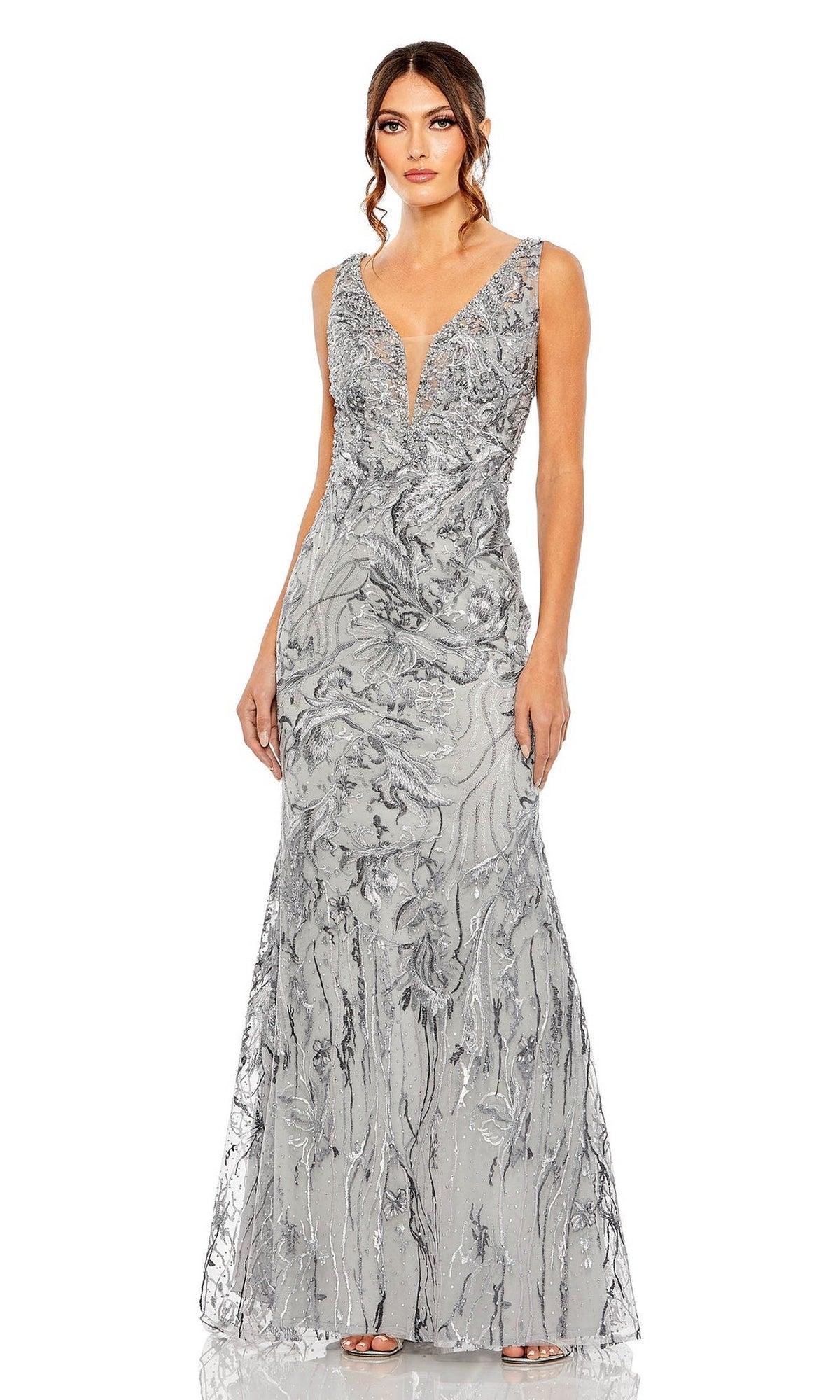 A woman wearing the Long Formal Dress 20484 by Mac Duggal, a silver, sleeveless, floor-length gown with a deep V-neckline and intricate sequin detailing, stands against a white background.